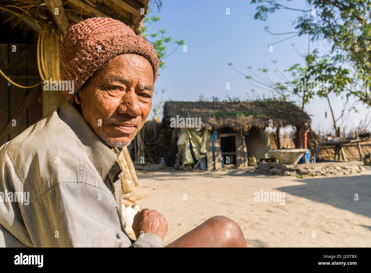 Portait of a local man, sitting in front of a typical farm house in the village Pandavnagar in Chitwan National Park Stock Photo