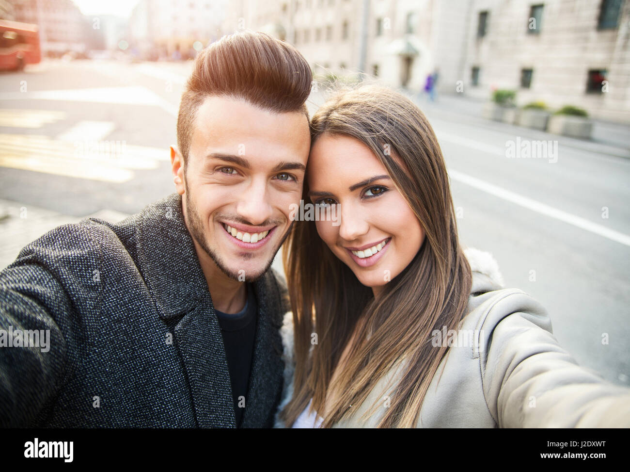 Happy young couple taking selfie by mobile phone on street. Beautiful couple selfie, love and fun concept. Toned photo, Close up portrait. Stock Photo