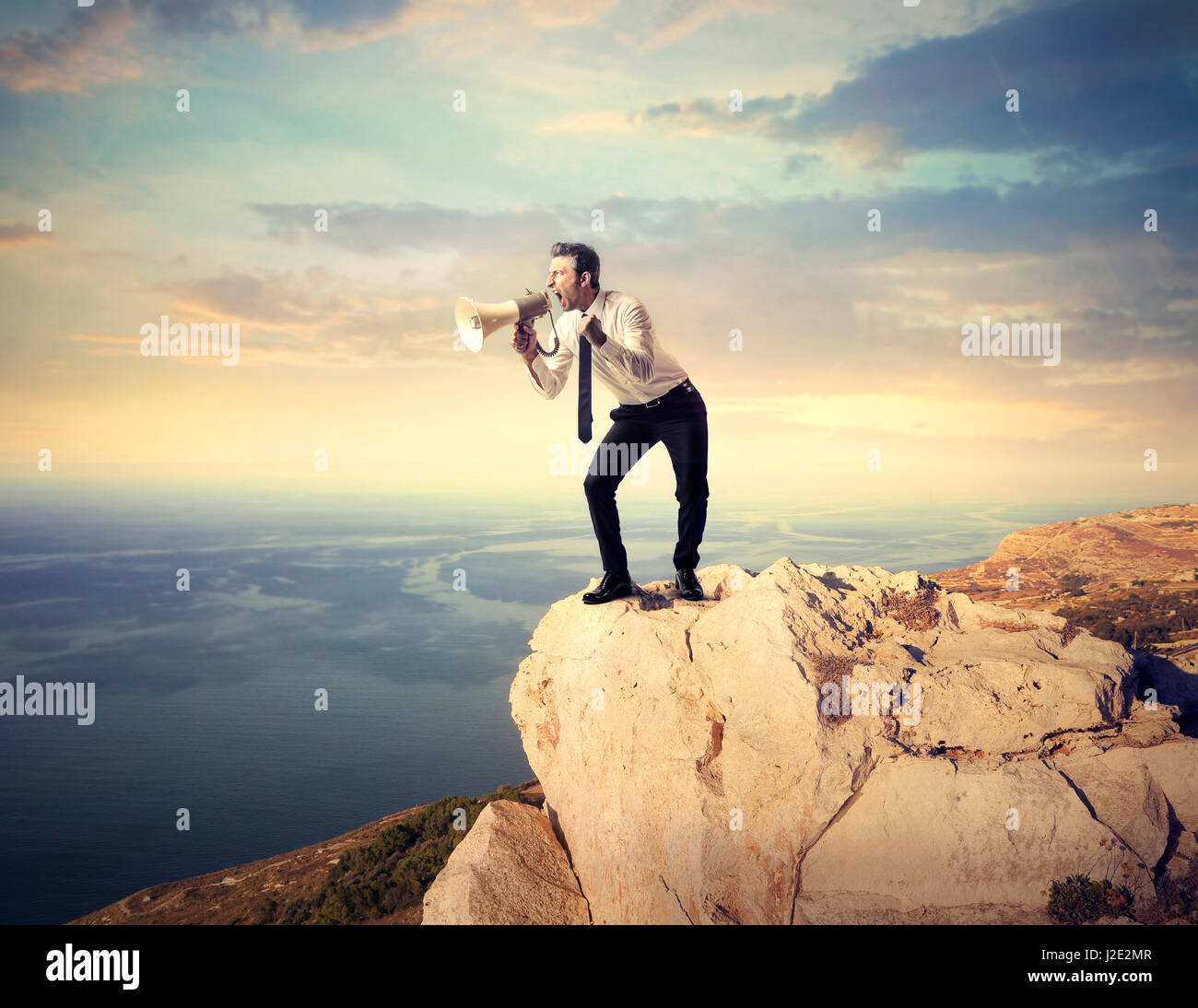 Businessman with megaphone on cliff Stock Photo