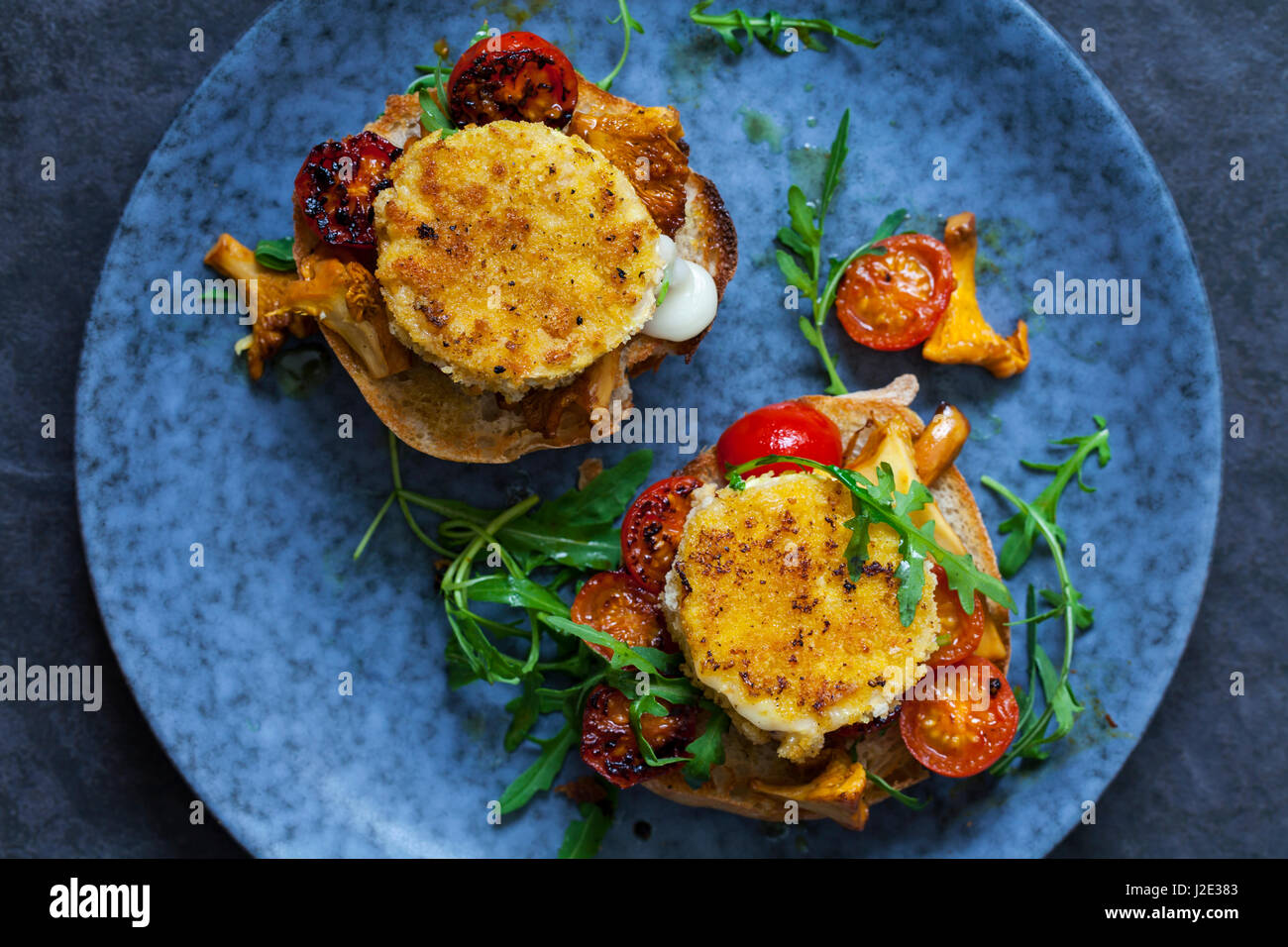 Baked goat cheese on sourdough bread with chanterelle mushrooms and cherry tomatoes Stock Photo