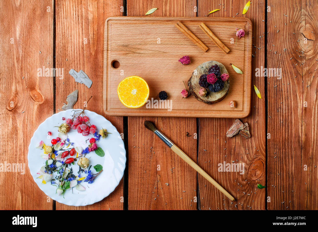 Art conceptual photo with flowers, brush, fruit spices  on a plate on a wooden background. Top of view. Stock Photo