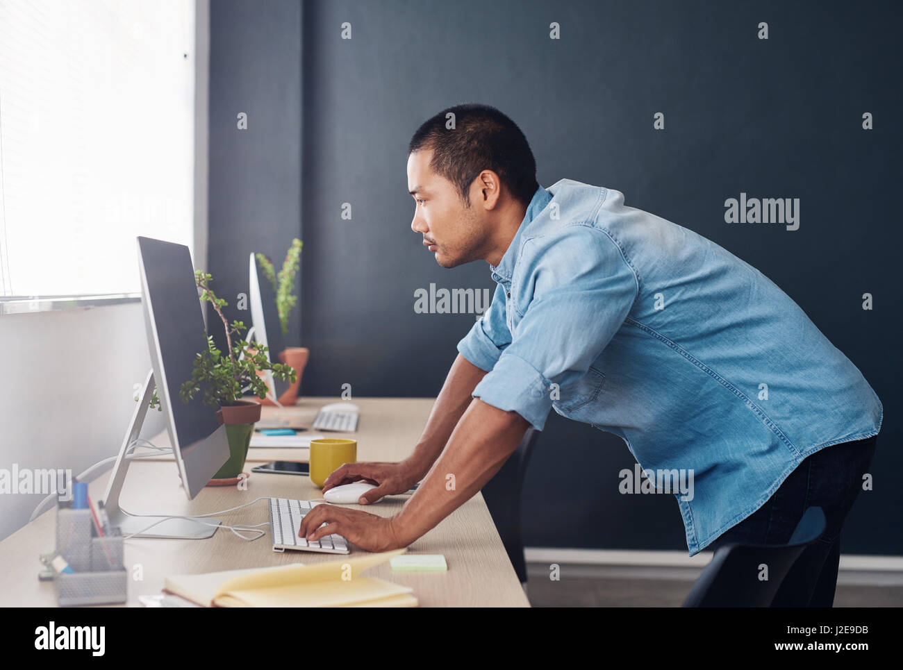 Young Asian designer standing at his desk using a computer Stock Photo