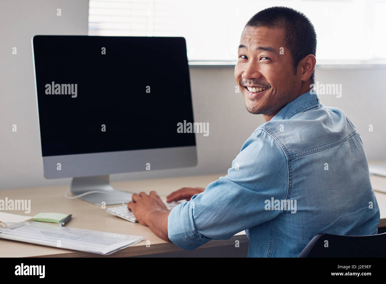 Happy young Asian entrepreneur at work on an office computer Stock Photo