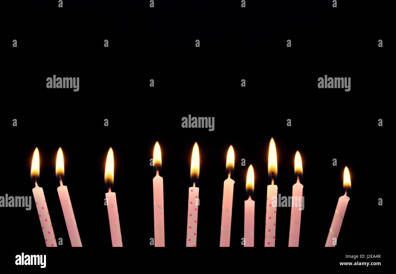 10 celebration pink candles, lit, against a black background
