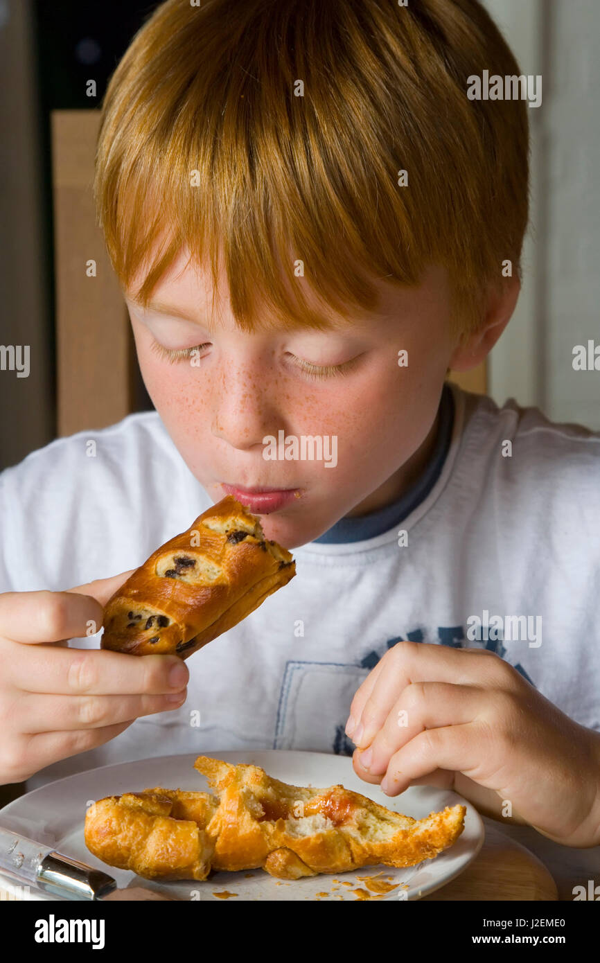 8 year old boy eating croissants, Gloucestershire, UK Stock Photo