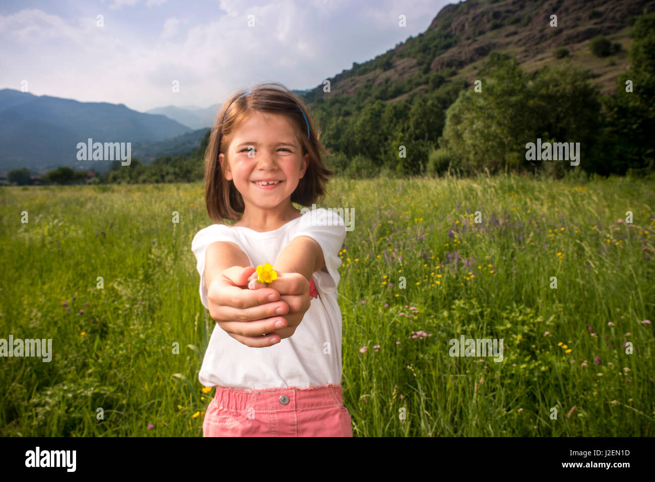 Young Girl Standing in Field Holding Flower Stock Photo