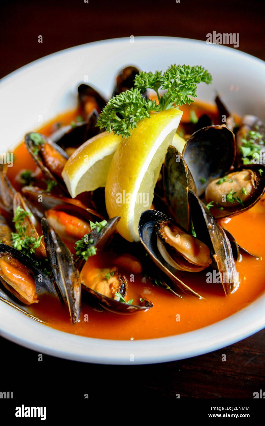 A bowl of mussels with their shells in a tomato sauce with lemon and parsley Stock Photo