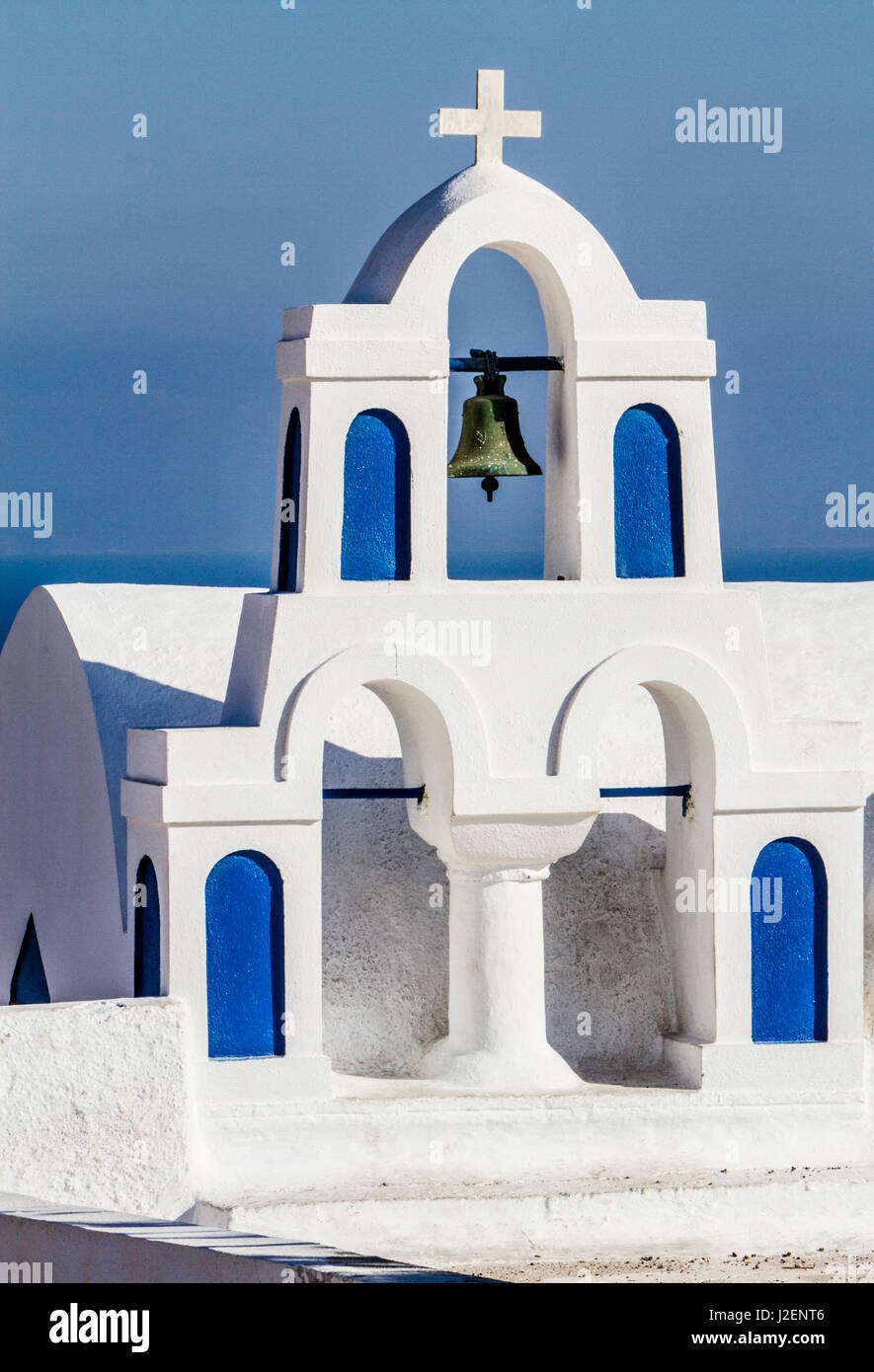 Oia, Greece. Greek Orthodox Church steeple, cross, bell, and blue arches against Aegean Sea Stock Photo