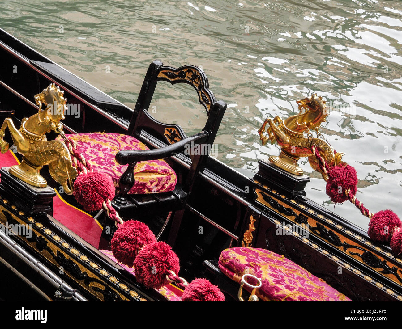 Venice, Italy. Gondola interior adorned with a golden horse serpent, velveteen cushions, black chair, on a canal Stock Photo