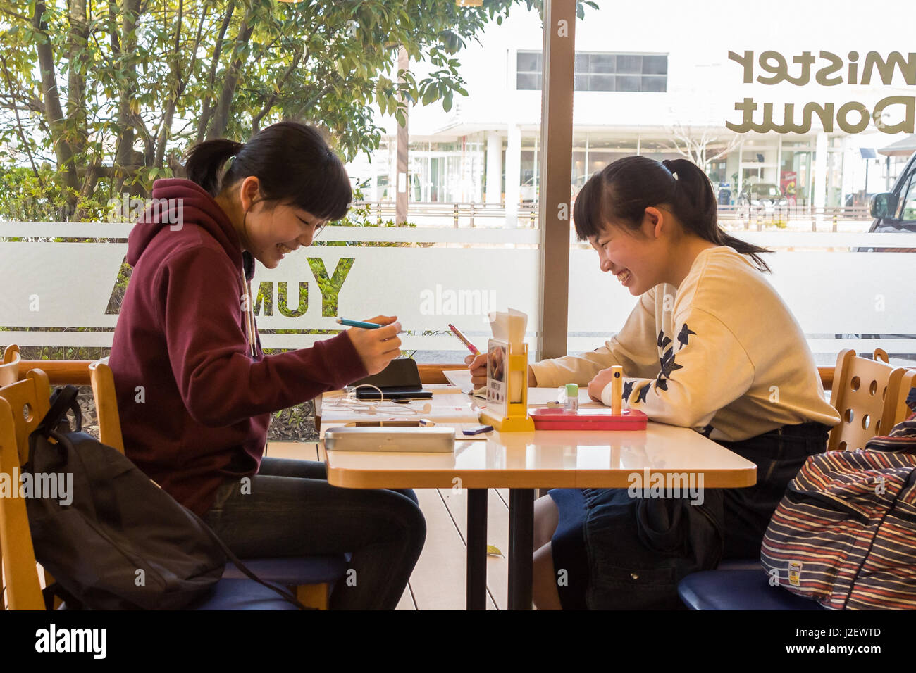 Kanazawa, Japan - March 30th, 2017: Japanese students girls sitting inside a Mister Donut coffee shop speaking and laughing. Stock Photo