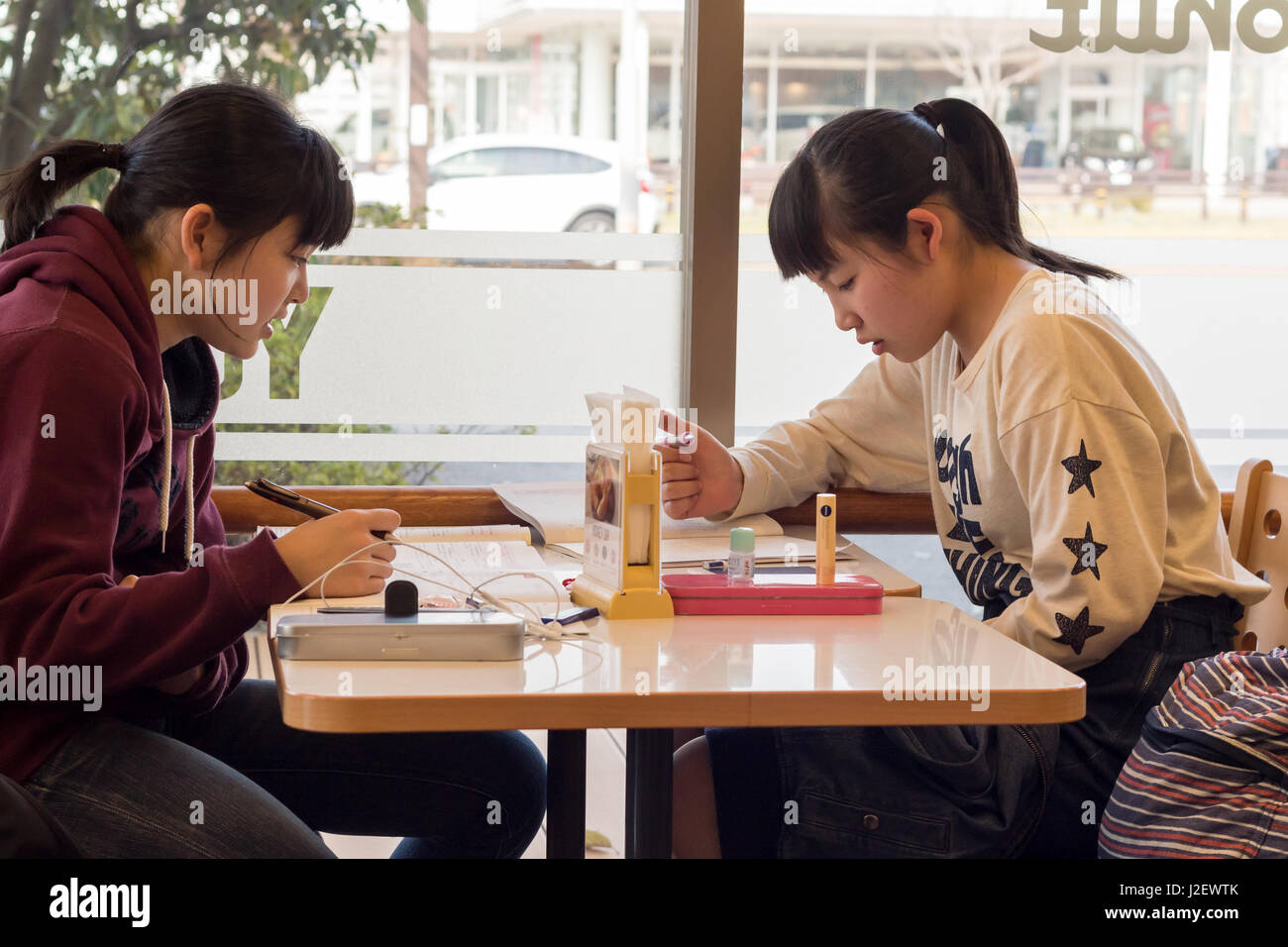 Kanazawa, Japan - March 30th, 2017: Japanese students girls sitting inside a Mister Donut coffee shop reading, studing. Stock Photo