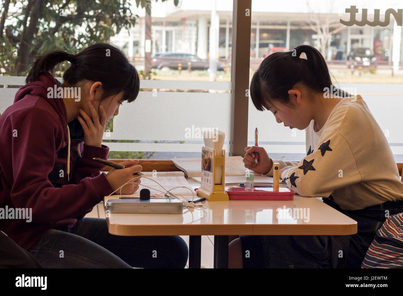 Kanazawa, Japan - March 30th, 2017: Japanese students girls sitting inside a Mister Donut coffee shop reading, studing. Stock Photo