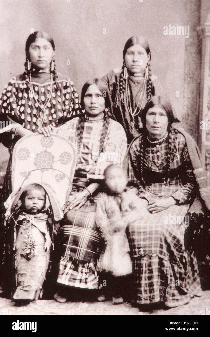 Historic black and white sepia toned Native American family of women dressed in traditional regalia with a young child and baby in papoose cradleboard. Stock Photo