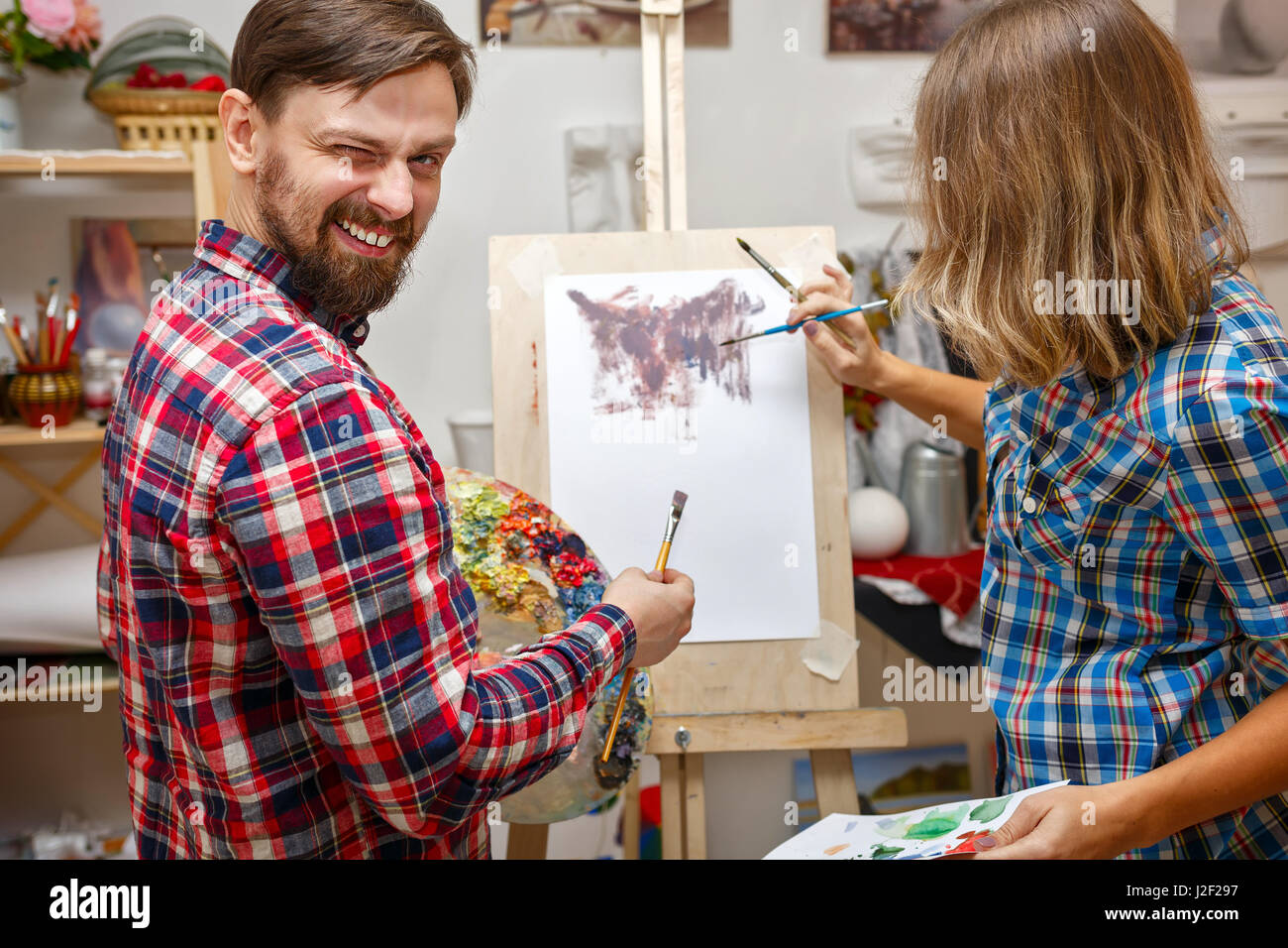 Students fool around in art school. A man and a girl draw an abstract painting with oil paints. Courses of drawing for adults. Stock Photo