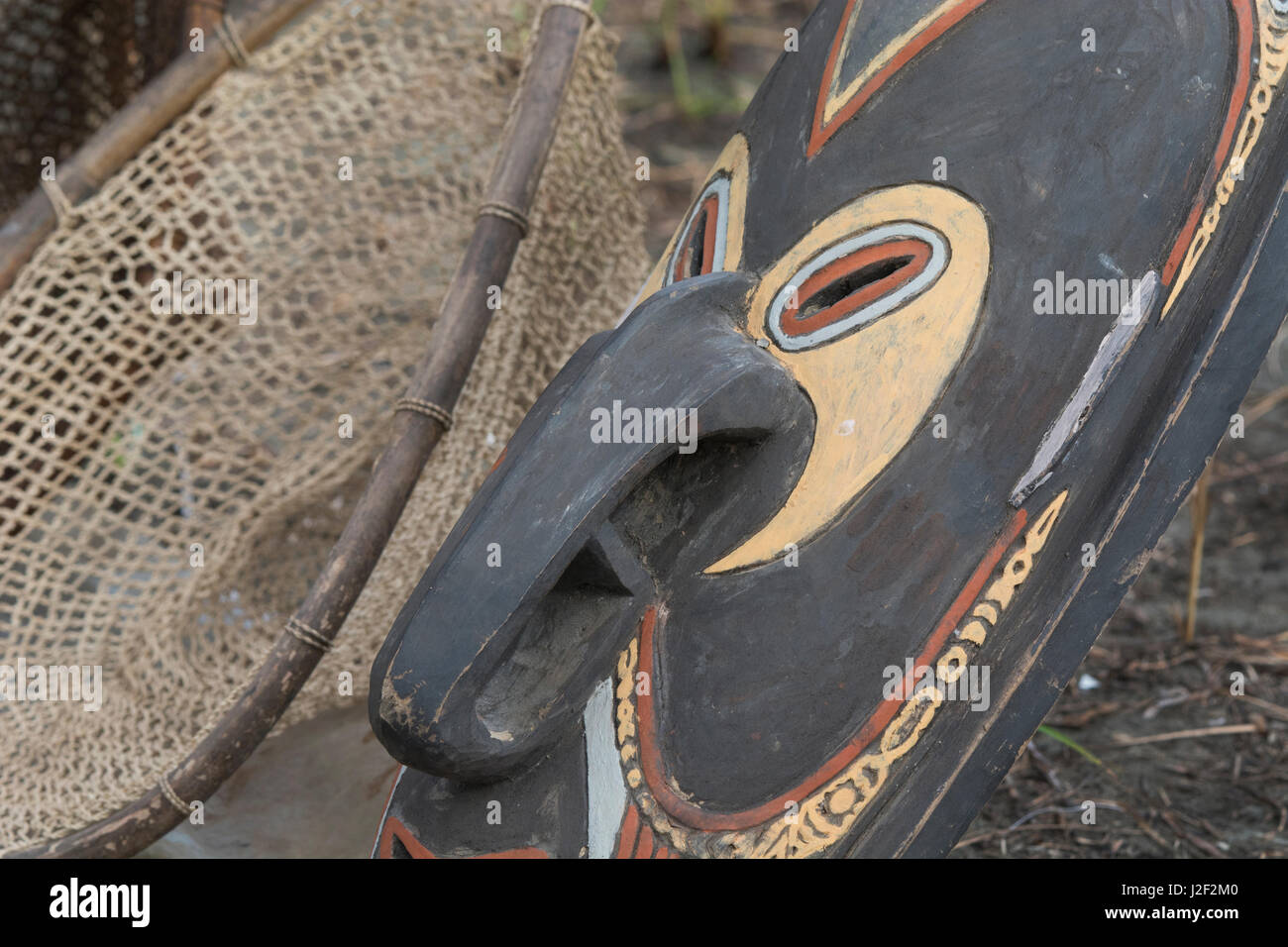 Melanesia, Papua New Guinea, Sepik River area, Murik Lakes, Karau Village. Traditional carved wooden mask that the area is famous for, woven basket in the distance. Stock Photo