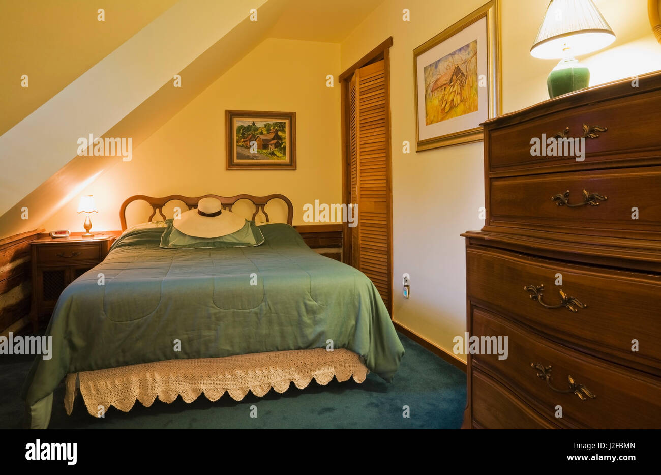 Queen size bed and old wooden dresser in guest bedroom on the upstairs floor inside a 1976 reconstructed cottage style log home Stock Photo