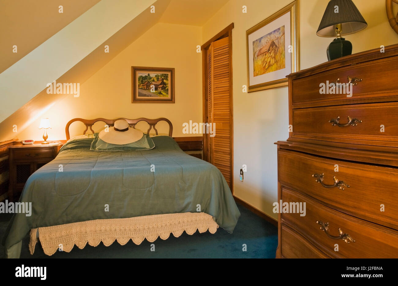Queen size bed and old wooden dresser in guest bedroom on the upstairs floor inside a 1976 reconstructed cottage style log home Stock Photo