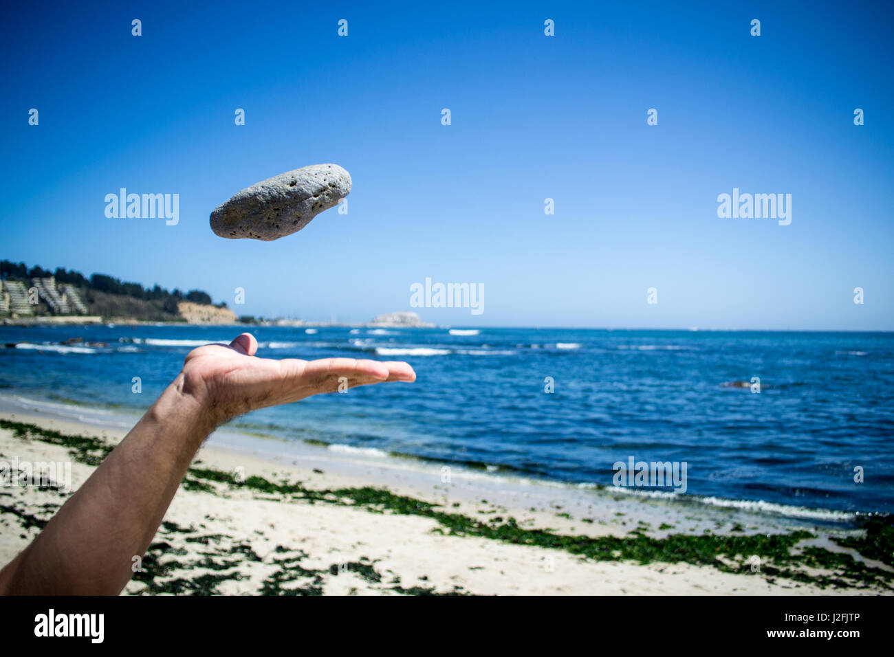 Hand throwing a stone in the air with beach as background Stock Photo
