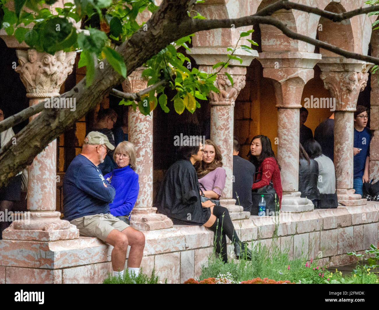 Perched on a wall with columns, multiracial visitors of different ages enjoy the Cuxa Cloister garden at The Cloisters Museum, a restored medieval monastery in Ft. Tryon Park, New York City. Stock Photo