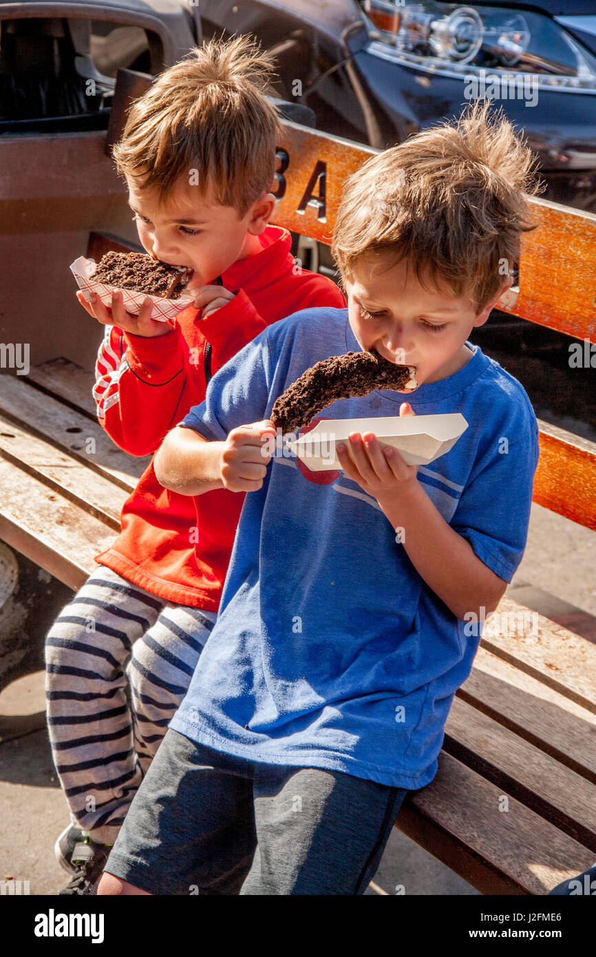 Two hungry brothers eat chocolate covered frozen bananas on a sidewalk