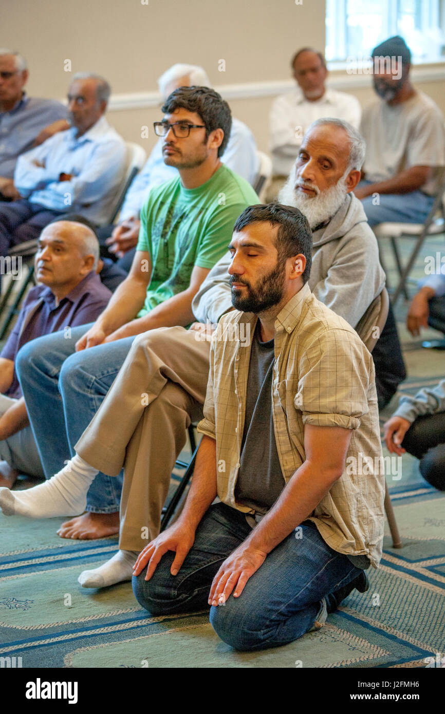 Listening to an Iman's sermon or Khutbah, Muslim men gather for Friday afternoon Abrahamic prayers during religious services at an Anaheim, CA, mosque. Note Islamic pattern carpet. Stock Photo