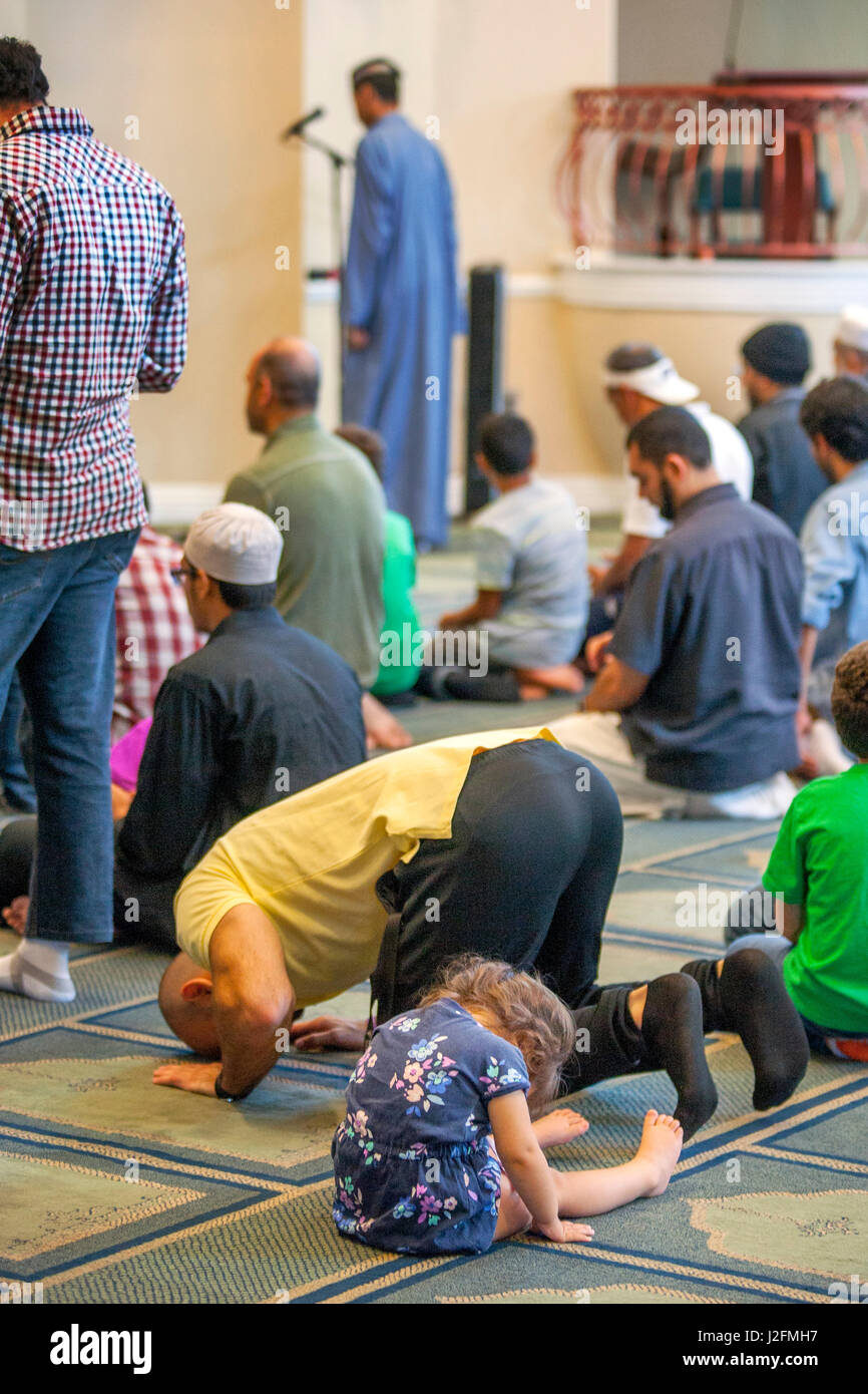 Muslim men prostrate themselves in 'Sujood' prayer position with their faces on the Islamic patterned carpet at Friday afternoon prayers during religious services at an Anaheim, CA, mosque. Note toddler daughter joining prayers. Stock Photo