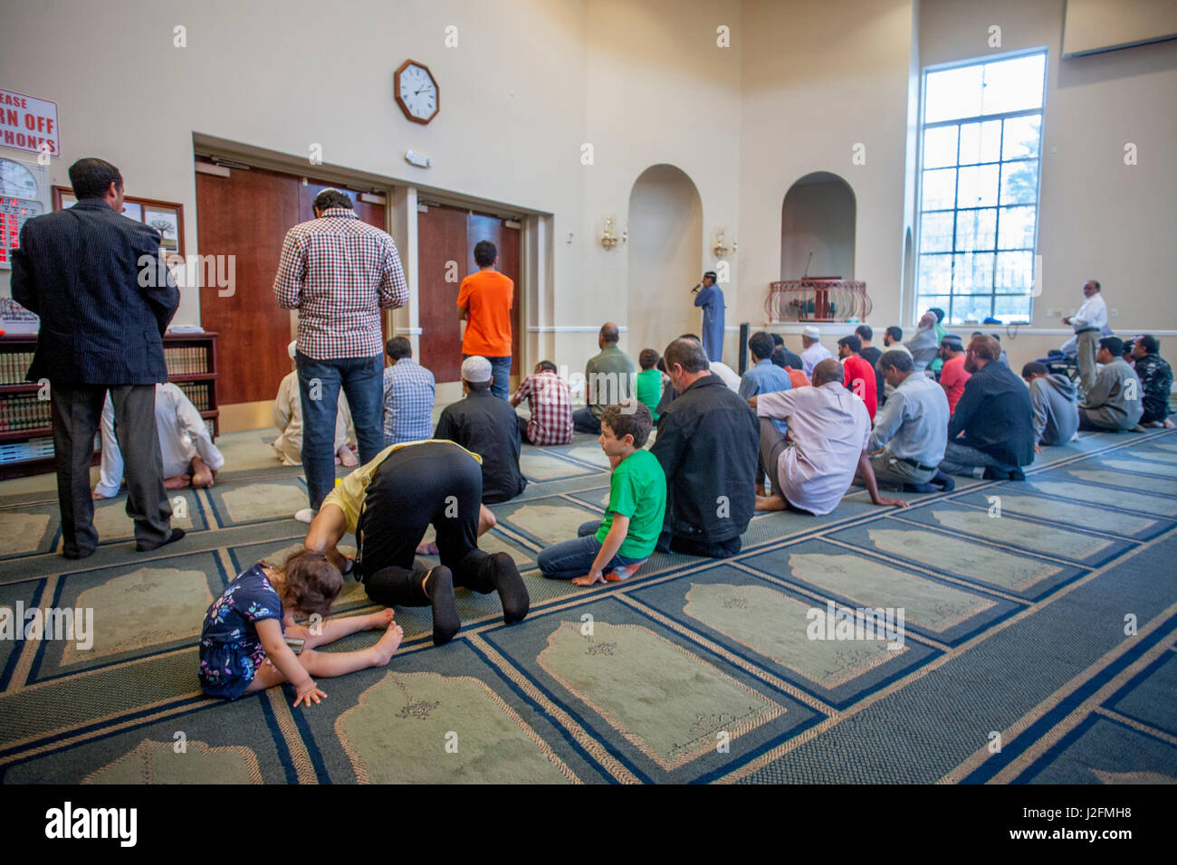 Muslim men prostrate themselves in 'Sujood' prayer position with their faces on the Islamic patterned carpet at Friday afternoon prayers during religious services at an Anaheim, CA, mosque. Note girl and boy worshippers. Stock Photo