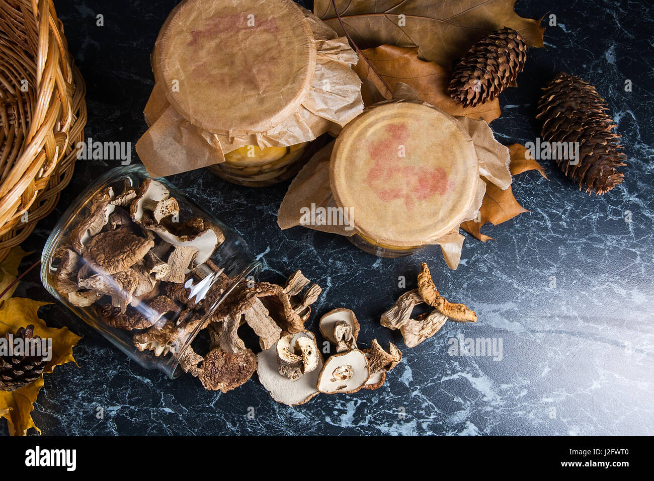 Two glass jars with wild mushrooms on black marble background. One jar
