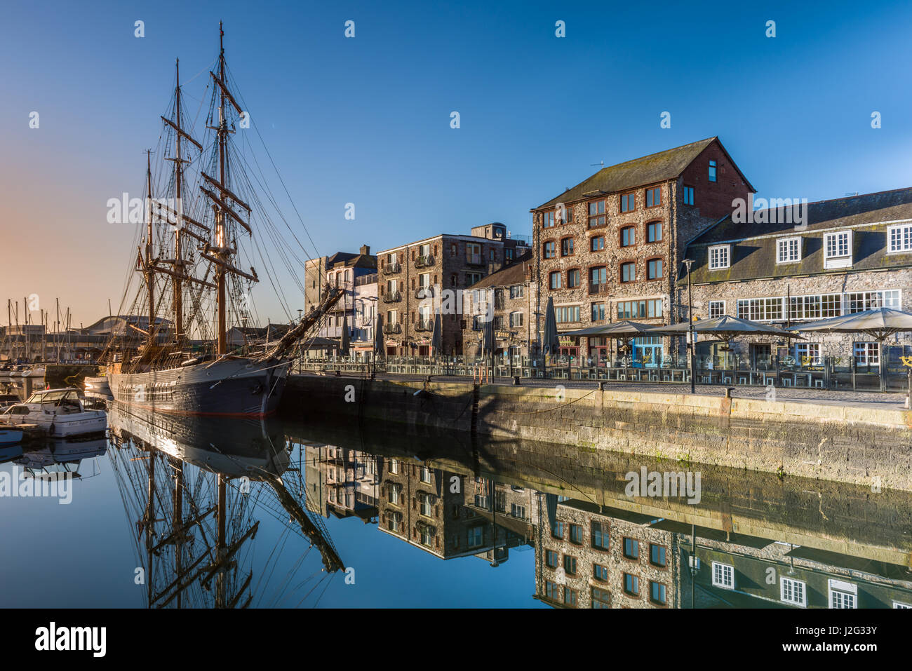 The early morning sunshine lights up a tall ship moored alongside the quay at the Barbican in Plymouth, South Devon. Stock Photo