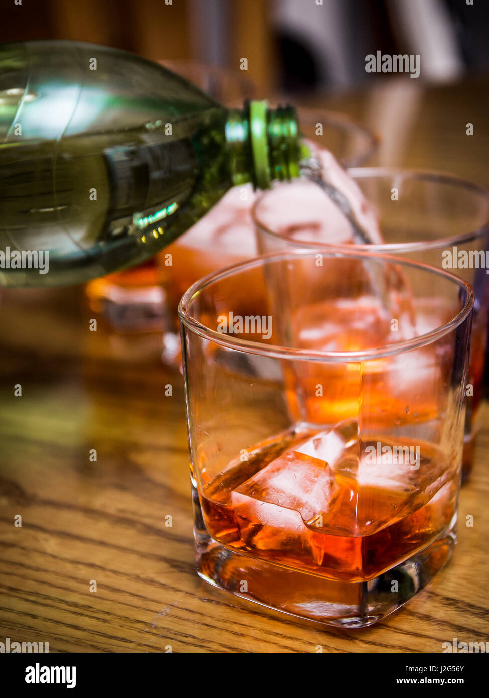 Mixing soft drink with alcohol, pouring into a glass tumbler with ice and a red colored drink in a bar Stock Photo