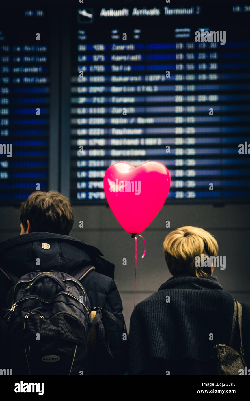 A couple wait for somebody in the Arrivals section of Munich Airport (MUC) with a pink heart shaped balloon. Stock Photo