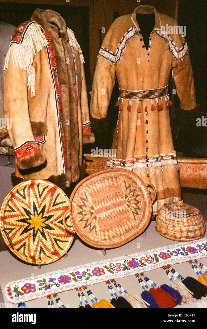 Traditional Athabaskan clothing made from moose hide decorated with fur trim and beadwork. Baskets and beaded belt strip compliment the museum display. Alaska Stock Photo
