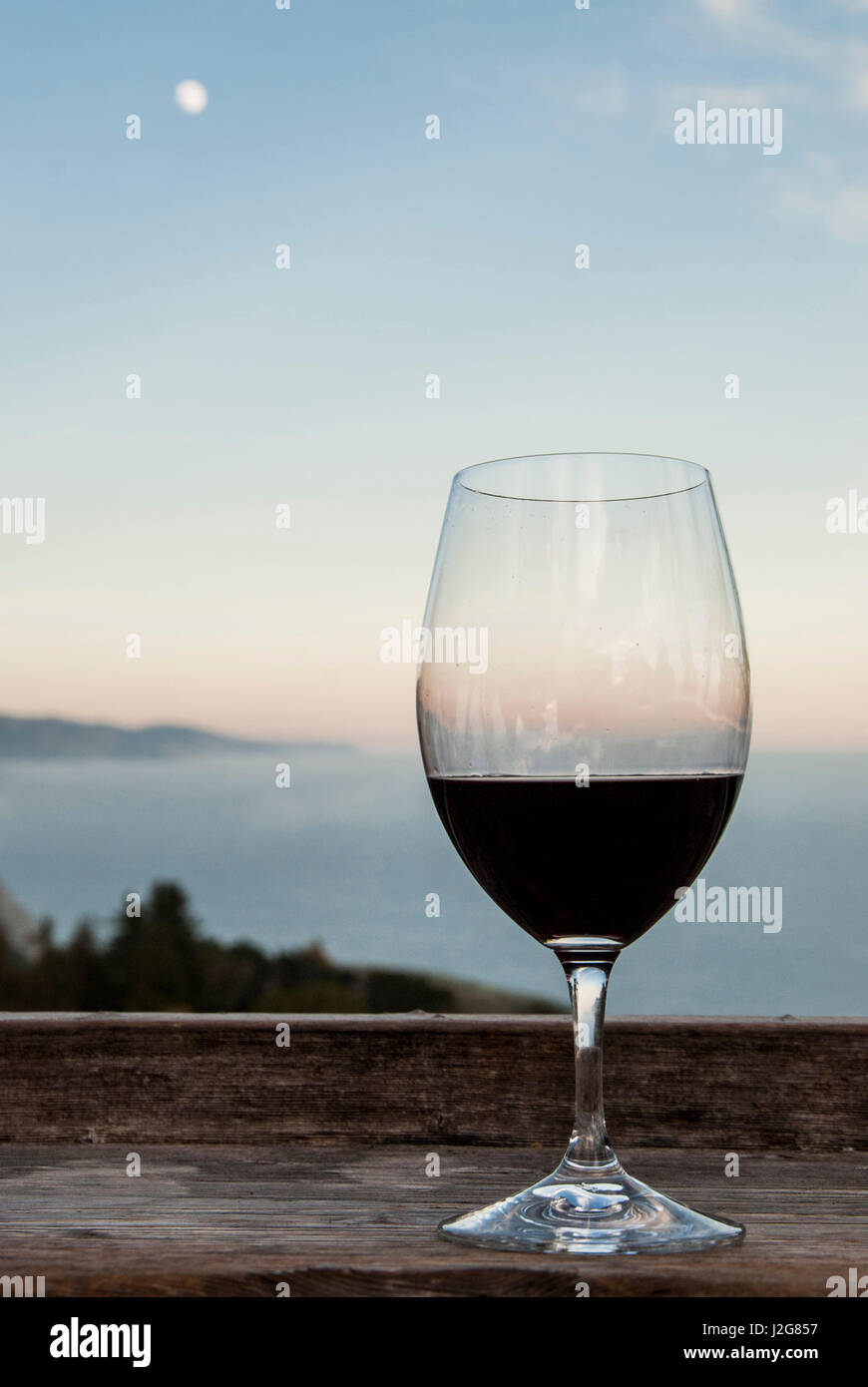 USA, California, Big Sur, Nepenthe restaurant, view of Lucia Mountains, Pacific Ocean, glass of red wine and full moon Stock Photo