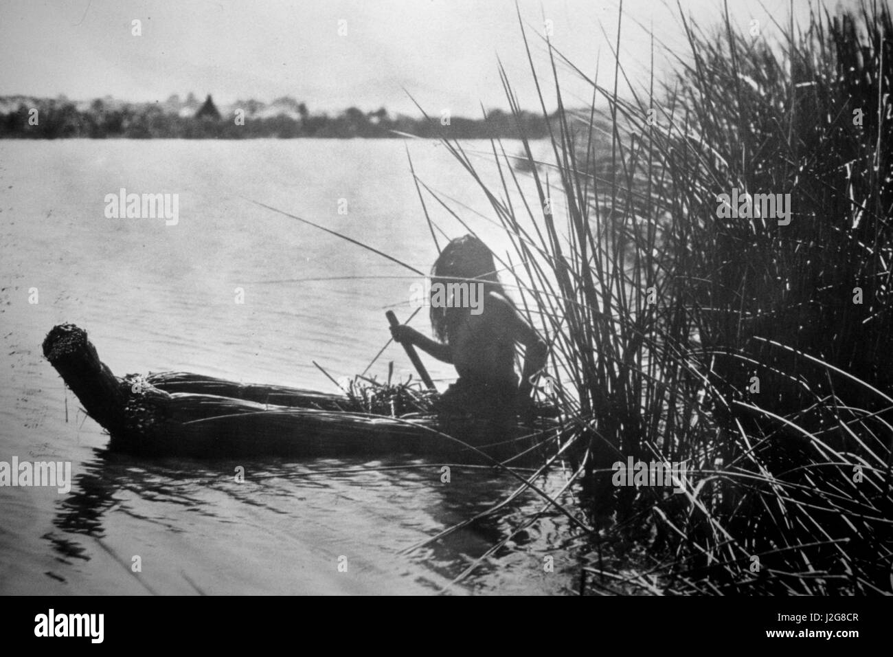 Historic black and white photograph of a Pomo fisherman paddling a canoe made from Tule reeds on Clear Lake, California Stock Photo