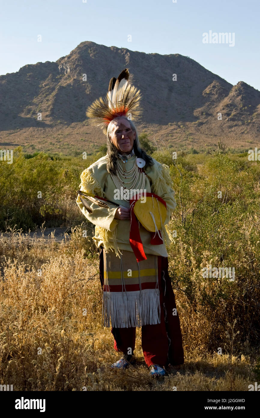 American Indian man, of the Sioux Nation, dressed in traditional outfit of  a ghost dance shirt, roach headdress, pony beads, breechcloth apron,  leggings and moccasins with a mountain in the background (MR