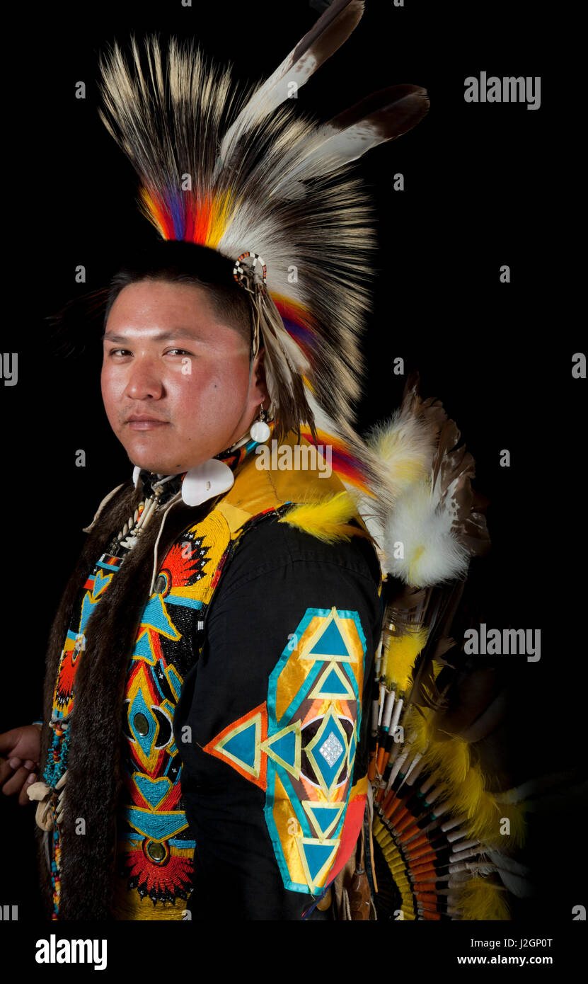 Traditional pow wow dancer, Carlton Yazzie (Dine aka Navajo), dressed in colorful regalia of a roach headdress, beaded vest and eagle feather bustle holds a wooden coup stick Stock Photo