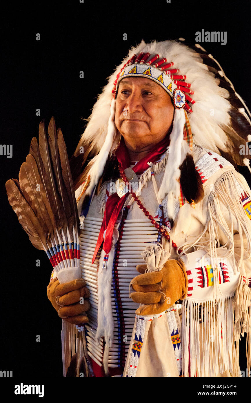 Jonas Grant (Ute, Navajo, Apache) dressed in eagle feather headdress war  bonnet and deerskin jacket decorated with beadwork holds a dance fan next  to a black background Stock Photo - Alamy