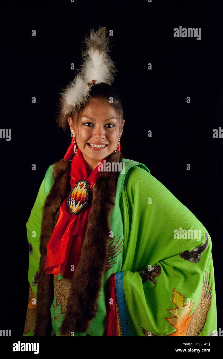 Native American Young Woman dressed in fancy shawl pow wow regalia poses against a black backdrop Stock Photo