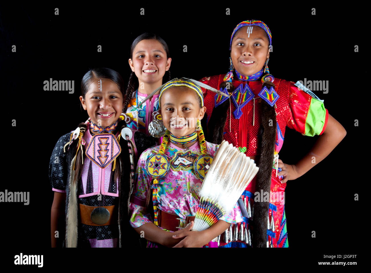 Pow wow friends Aarora Piper, Jaydean, Bailee and Shandiin Horton all dressed in dance regalia pose as a group against a black background Stock Photo