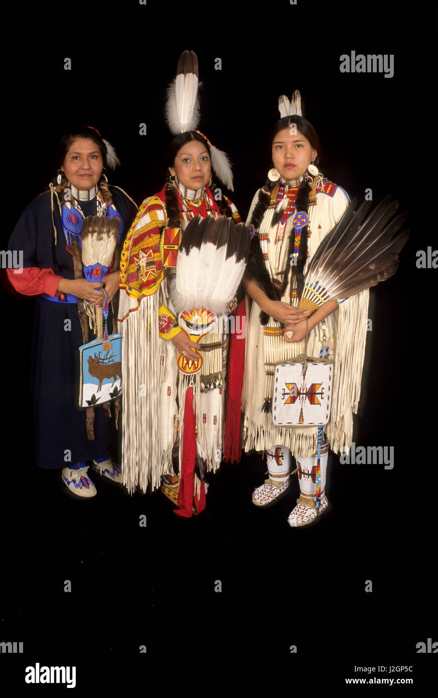 Native American family of mother in a trade cloth dress with teenage daughter who is dressed in traditional regalia and a woman who is a sister and auntie. (MR) Stock Photo