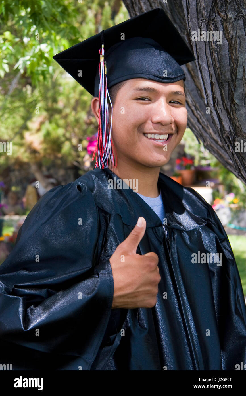 Native American young man dressed in cap and gown gives a thumbs up during his graduation ceremony. (MR) Stock Photo