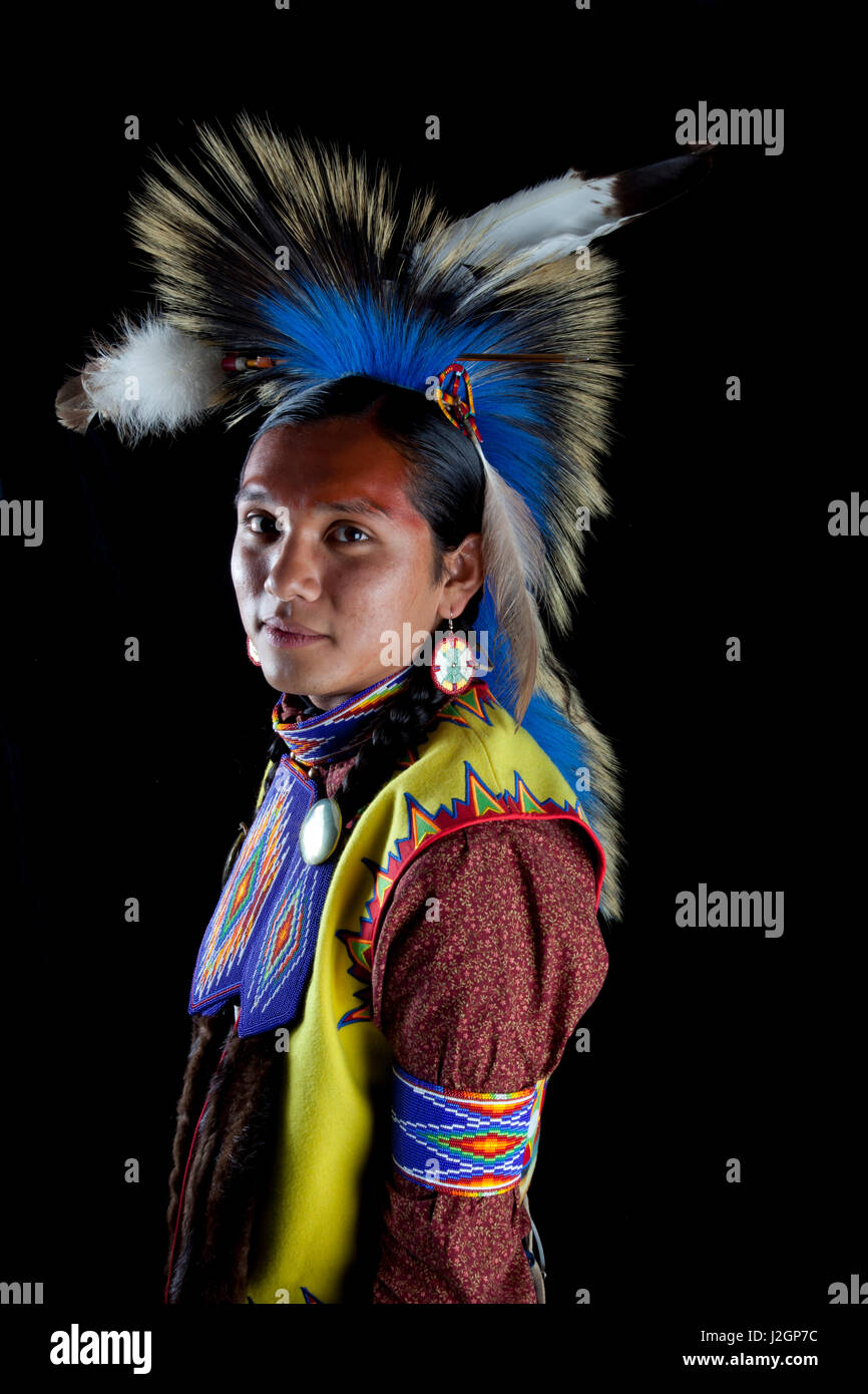 Traditional teenage boy dressed in pow wow regalia with beadwork and a roach headdress in front of black backdrop. Ian Stevens Stock Photo