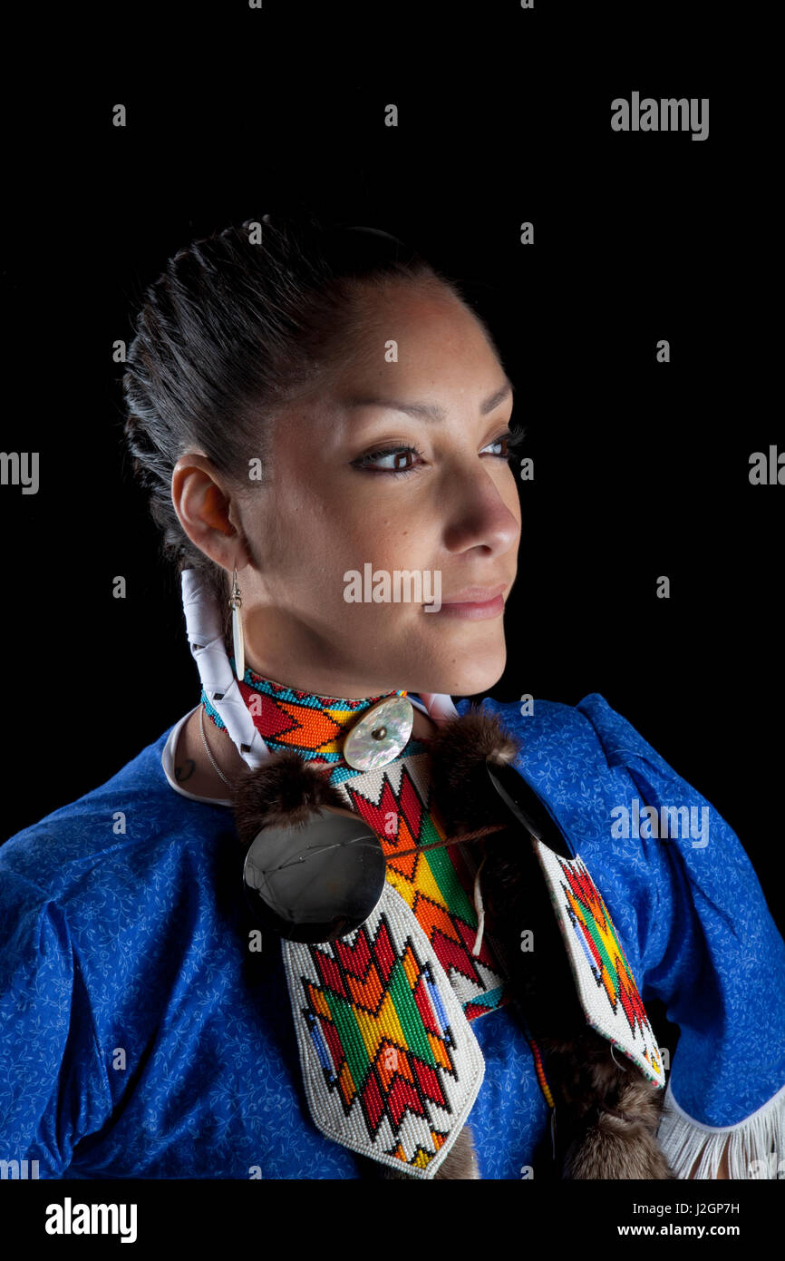 Traditional teenage girl, Challis Baldwin (Shoshone-Bannock), dressed in pow wow jingle dancer dress and beadwork poses on a black backdrop. Stock Photo