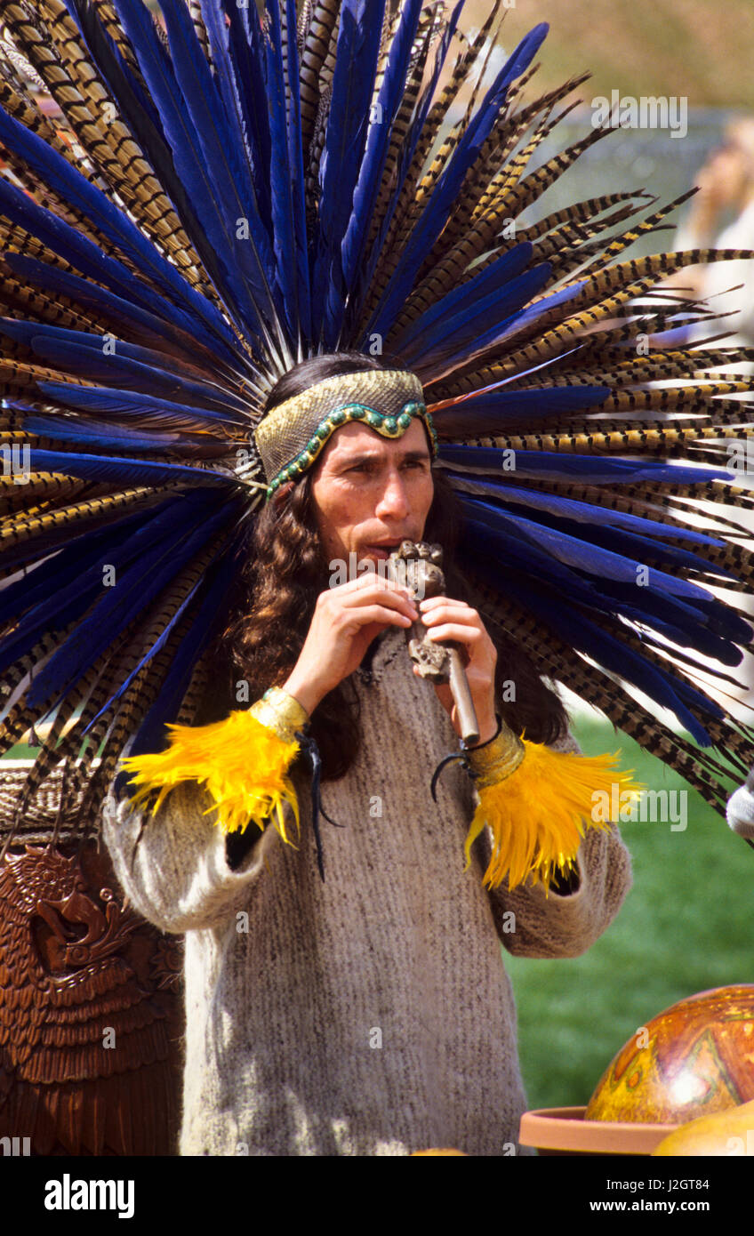 Aztec man dressed in traditional headdress and snake headband plays a traditional wooden whistle flute during a musical presentation in Malibu Beach, CA Stock Photo