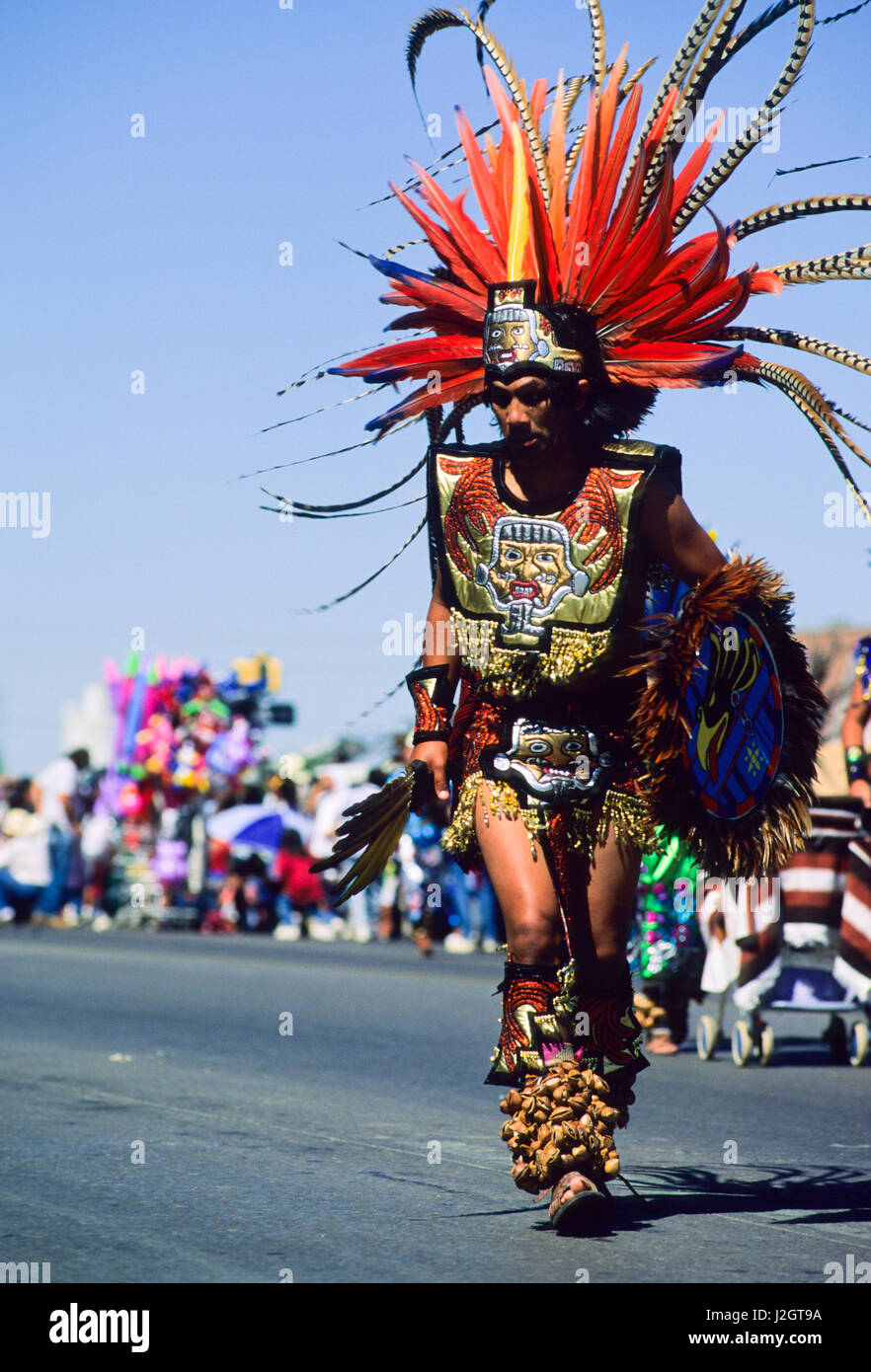 Aztec man wears traditional large headdress made from long colorful feathers, a decorative chest plate, breechcloth and leg rattles during an Inter-tribal parade in Gallup New Mexico Stock Photo