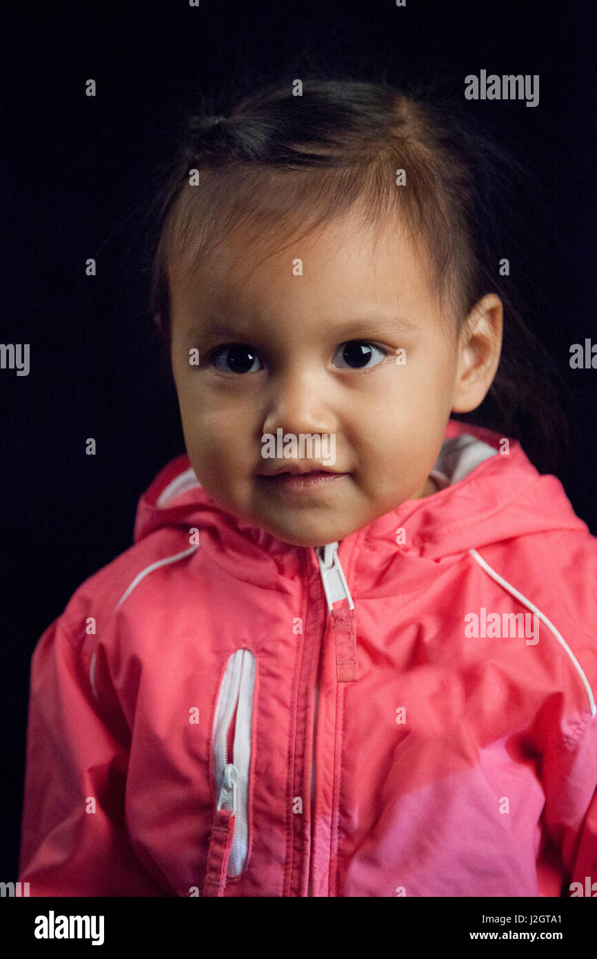 Contemporary Native American girl at toddler age in pink jacket next to black backdrop. Harmony Lahr (Blackfoot, Navajo) Stock Photo