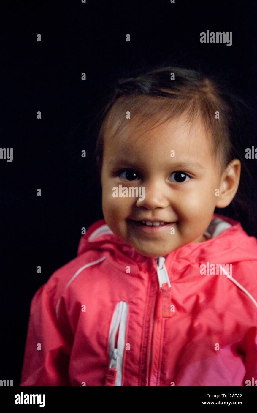 Contemporary and happy healthy Native American girl at toddler age in pink jacket next to black backdrop. Harmony Lahr (Blackfoot, Navajo) Stock Photo