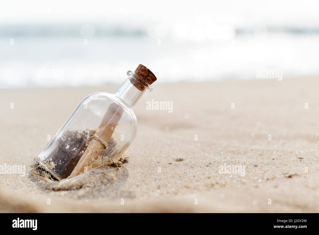 closeup of a glass bottle with a rolled message inside stranded in the sand of a lonely beach Stock Photo