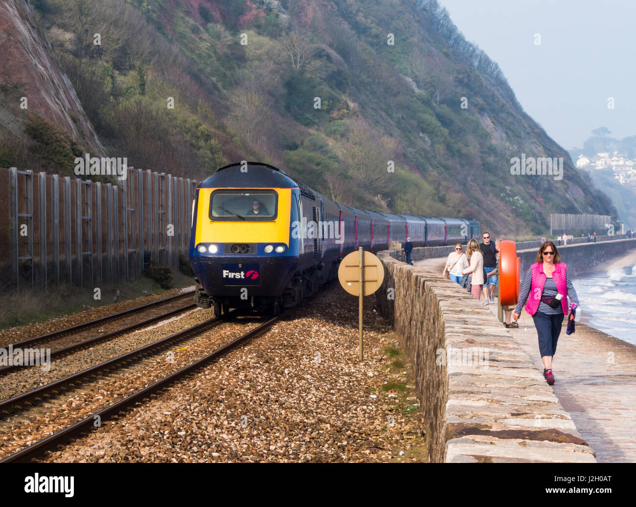 A train passes walkers on Teignmouth sea front. Stock Photo