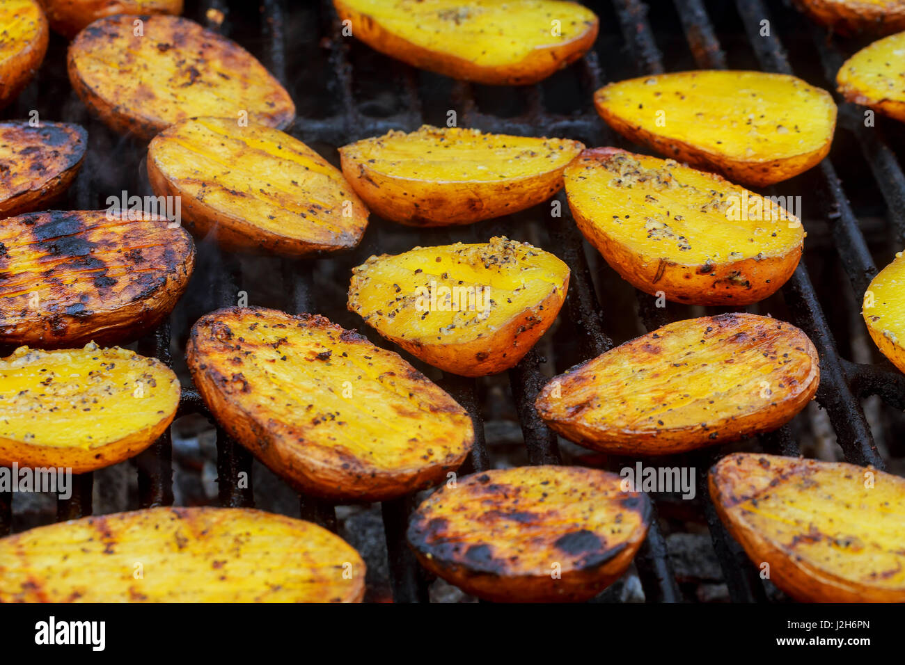 Grilling delicious potatoes on barbecue. Slice potatoes are prepared on the grill on sunny day. Close up. Culinary concept. Stock Photo